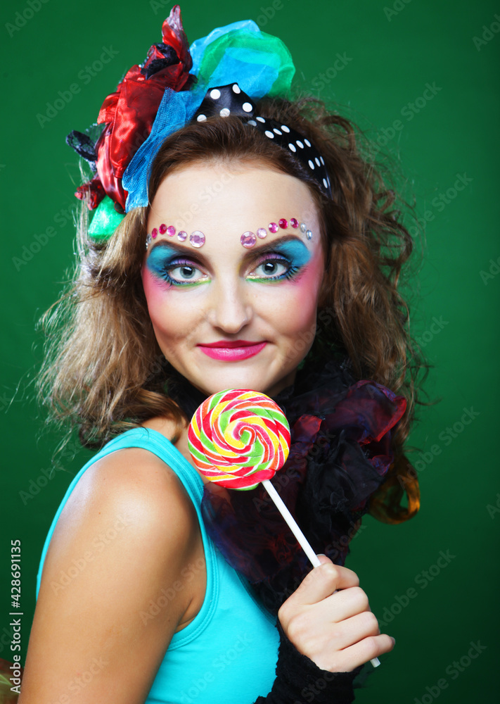 Portrait of young woman in carnaval with creative make-up holding a big candy . Doll style. Stock Photo | Adobe Stock