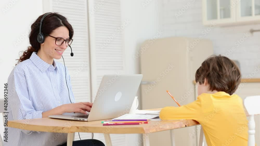 Mom work remotely with small son from kitchen. Young businesswoman home office with little boy draw during important business call via video conference. Smiling mother talk with partners online Mom work remotely with small son from kitchen. Young businesswoman home office with little boy draw during important business call via video conference. Smiling mother talk with partners online