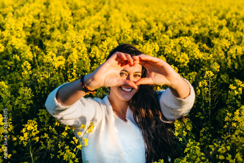 Young girl making the symbol of love in a field of rapeseed.