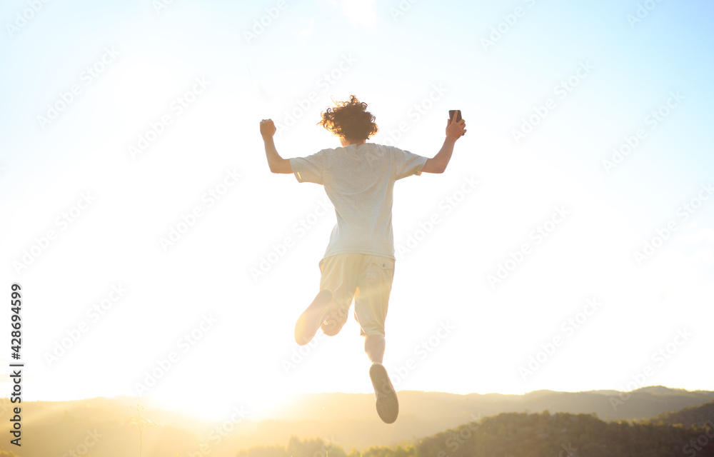 Man jumping and celebrating with arms raised with sunset in the background. Man jumping for joy, feeling happy and free. Man jumping and celebrating with arms raised with sunset in the background. Man jumping for joy, feeling happy and free.