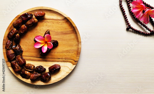 Ramadan background, dates heart shaped on a wooden plate and prayer beads on a cream background