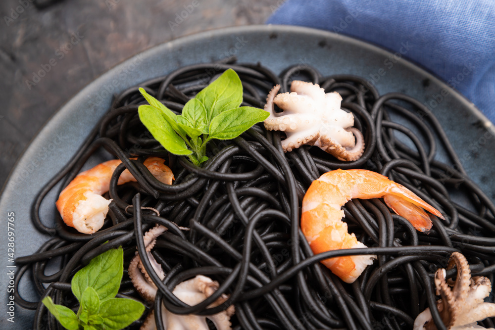 Black cuttlefish ink pasta with shrimps or prawns and small octopuses on gray wooden background. Top view, selective focus.