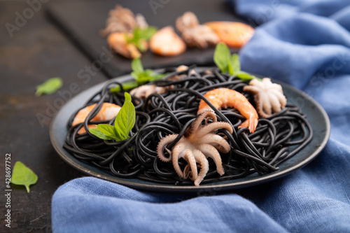 Black cuttlefish ink pasta with shrimps or prawns and small octopuses on gray wooden background. Side view, selective focus.