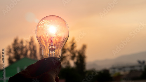 Solar power in nature concept light bulb hand held background with sunset evening