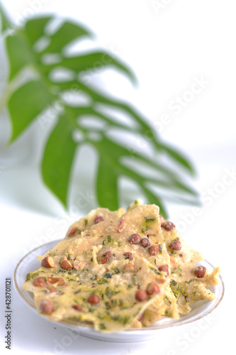 Peyek Kacang or peanut rempeyek in white plate. Deep fried savoury cracker made from rice flour and peanut. Indonesian traditional food. With monstera deliciosa leaf as a background photo