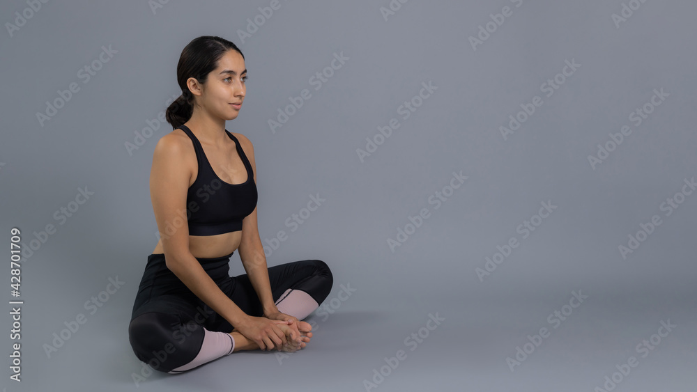 Fototapeta premium Joven mujer latina mexicana atleta instructora entrenando yoga dando calentamiento y estiramiento de musculos vestida de negro y haciendo ejercicio con fondo gris en pandemia por covid 19 coronavirus
