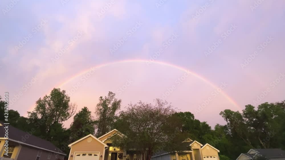 Vivid rainbow appears above residential neighborhood after storm, wide, 4k