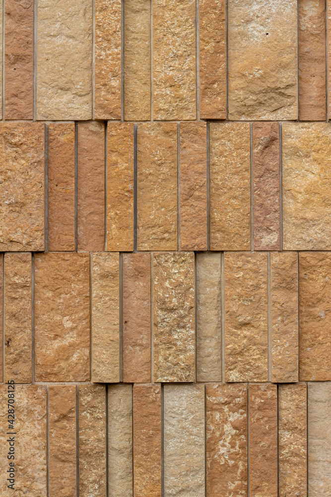 This image shows a rough texture stone wall background with attractive narrow vertical kasota limestone blocks in varying widths, and shades of brown and beige This image shows a rough texture stone wall background with attractive narrow vertical kasota limestone blocks in varying widths, and shades of brown and beige