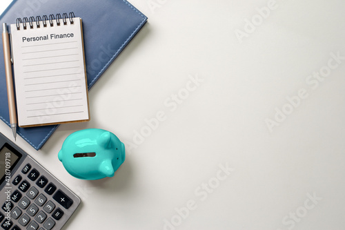Fotografie Notebook with text personal finance and pen, blue piggy bank, calculator, depict budget planning for basic needs, family, personal expense, Business and personal financial concept