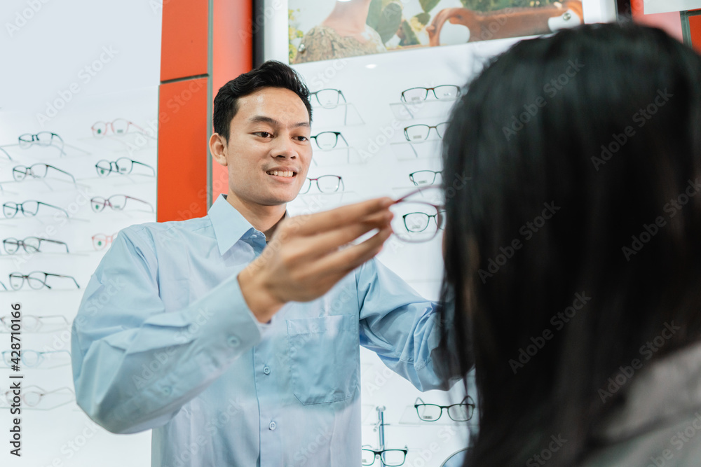 A male shop assistant serves and dresses a woman customer while she is in an optician A male shop assistant serves and dresses a woman customer while she is in an optician
