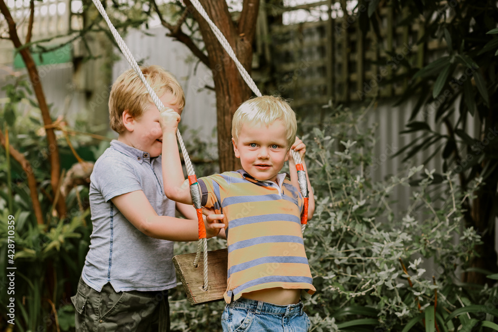 Fototapeta premium Beautiful happy brothers playing together on backyard swing set