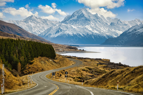 Asphalt road to the big and tall Mountains in winter, dry grass turns yellow in blue skies and beautiful clouds in the daytime in Mount cook National Park in southern island, New Zealand