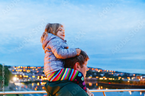 Beautiful portrait of cute little toddler girl with father. Happy baby child hugging with dad. Lovely family of man and daughter. Outdoors at the dusk. © Irina Schmidt