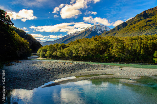A stream in the valley with great nature, high mountain background with snowy peaks, in the daytime blue sky and beautiful clouds, the nature trail in Haast New Zealand.