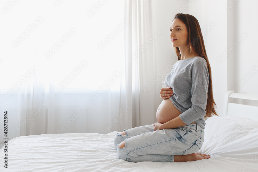 Young beautiful pregnant woman sitting on bed with white linen.