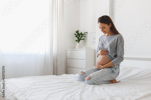 Young beautiful pregnant woman sitting on bed with white linen.