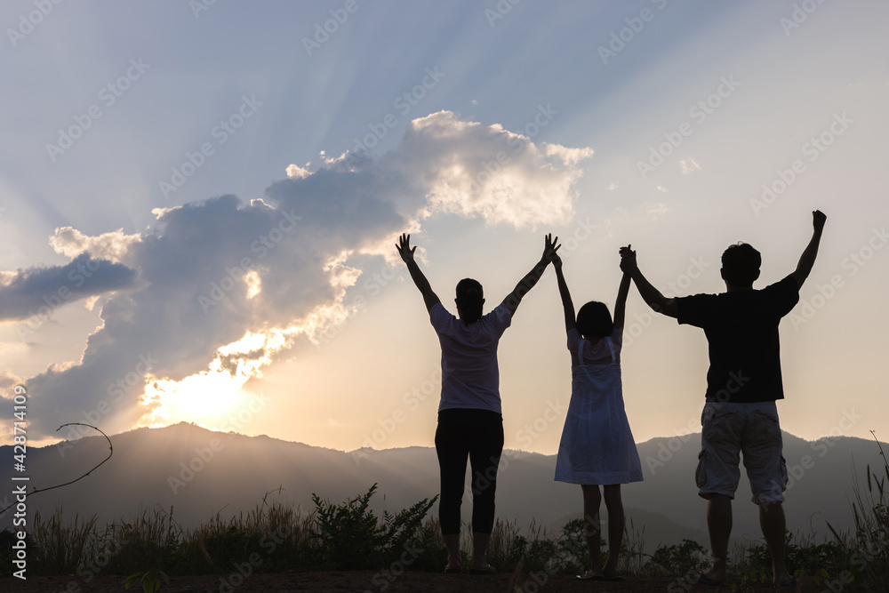 Silhouette of Joyful family stands with raised arms on the mountain at the sunset time. Silhouette of Joyful family stands with raised arms on the mountain at the sunset time.