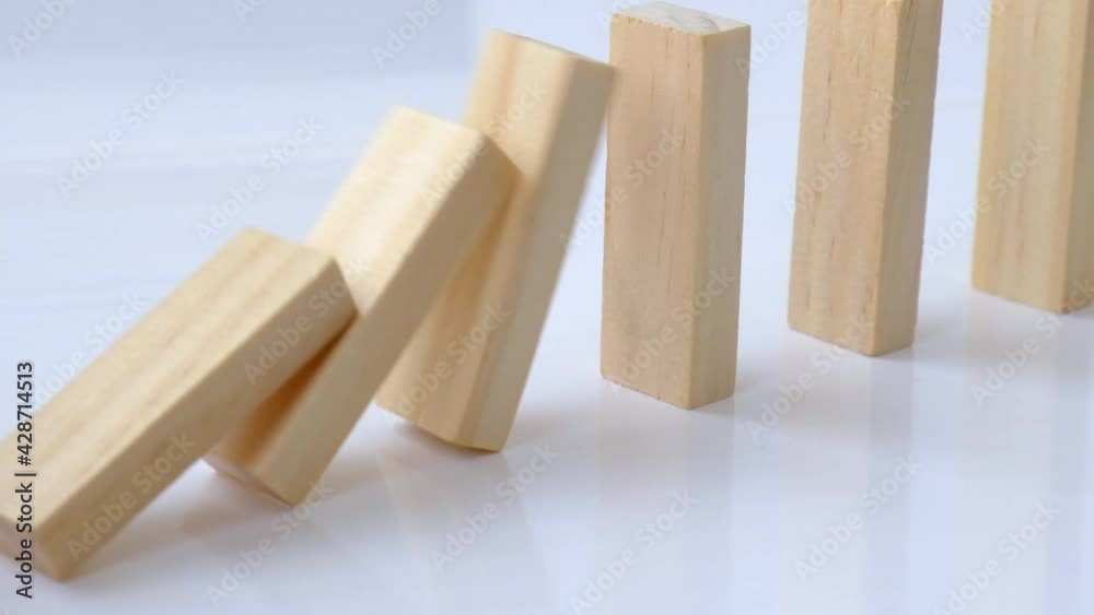 Domino effect, row of wooden domino falling down on white background. Dominoes falling in a row, hand pushes a Domino and starts a chain reaction Board game. Falling dominoes