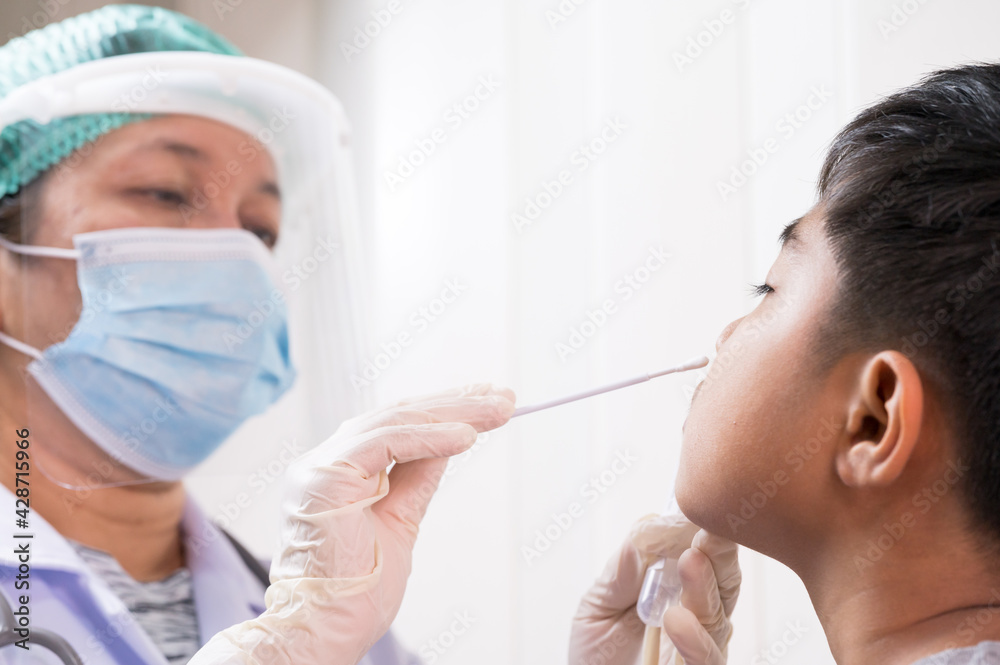 Naklejka premium Doctor taking a swab for corona virus sample from potentially infected Asian boy nose.Covid-19 laboratory test.Medical staff with PPE suit test covid-19 to asian kid by nose swab at hospital.