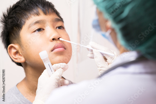 Doctor taking a swab for corona virus sample from potentially infected Asian boy nose.Covid-19 laboratory test.Medical staff with PPE suit test coronavirus to asian kid by nose swab at hospital.