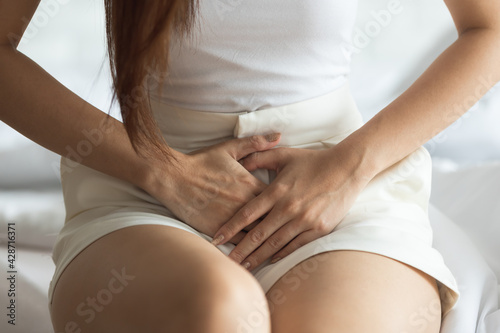 Attractive Asian woman sitting on bed have a bladder pain. photo
