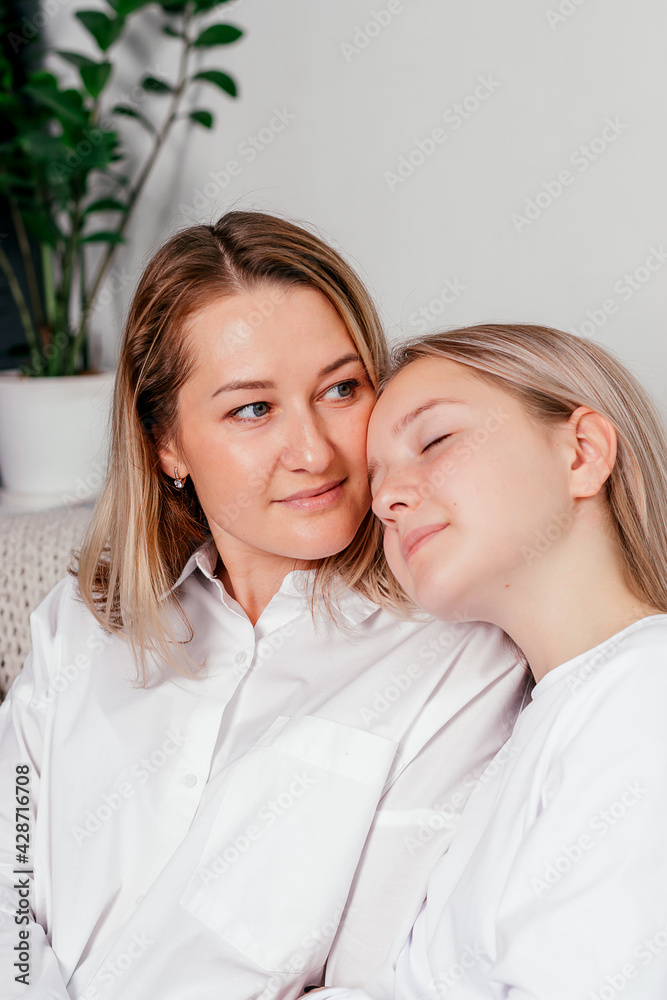 A mother and her teenage daughter are sitting on the couch at home, hugging each other and spending time together. Women's generation, International Women's Day, Happy Mother's Day. A mother and her teenage daughter are sitting on the couch at home, hugging each other and spending time together. Women's generation, International Women's Day, Happy Mother's Day.