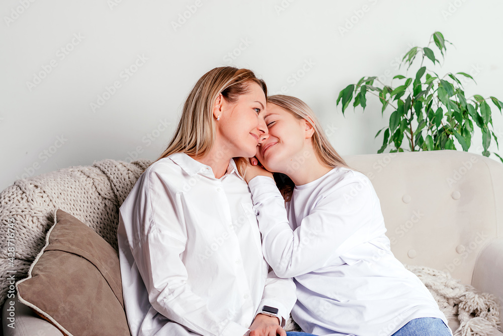 A mother and her teenage daughter are sitting on the couch at home, hugging each other and spending time together. Women's generation, International Women's Day, Happy Mother's Day. A mother and her teenage daughter are sitting on the couch at home, hugging each other and spending time together. Women's generation, International Women's Day, Happy Mother's Day.