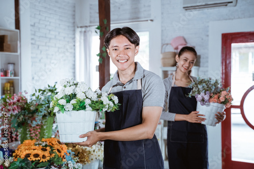 Obraz na płótnie happy young man florist wearing apron holding bucket flower smiling looking at camera