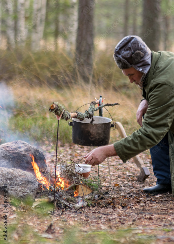 man in the forest trying to light a campfire, a tree branch with a pot over the campfire, blurred forest background, bonfire and smoke, autumn time man in the forest trying to light a campfire, a tree branch with a pot over the campfire, blurred forest background, bonfire and smoke, autumn time