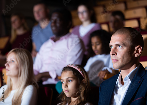Father, mom and daughter are carefully watching spectacle or concert in the theater auditorium