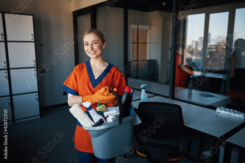 Pleased cleaning lady with janitorial supplies looking ahead photo