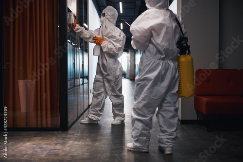 Two people in hazmat suits disinfecting the office corridor photo