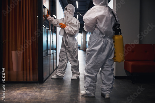 Canvas-taulu Two people in hazmat suits disinfecting the office corridor