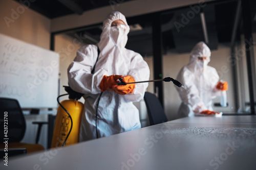 Trained janitorial staff sanitizing the surfaces of desks photo