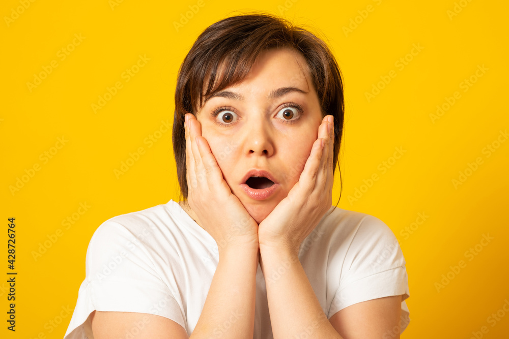 Happy woman grabs face, hears wonderful news, realises she won huge money, stands impressed and speechless, dressed in white t-shirt, feels lucky and thrilled, got incredible offer. Happy woman grabs face, hears wonderful news, realises she won huge money, stands impressed and speechless, dressed in white t-shirt, feels lucky and thrilled, got incredible offer.