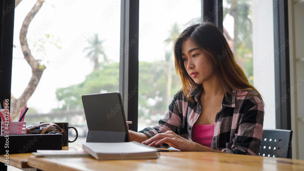 Young asian woman designer sitting near window in office and working with computer tablet. Young asian woman designer sitting near window in office and working with computer tablet.