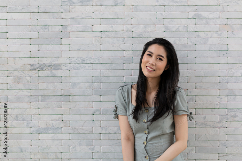 Portrait of a happy Asian girl in dress standing by the stone wall. Young traveling woman standing near stone wall during holiday. Tourist woman standing by the wall.