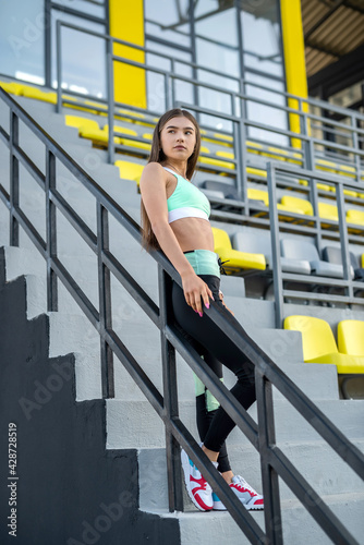portrait attractive girl in sports wear posing at stadium before fitness exercise