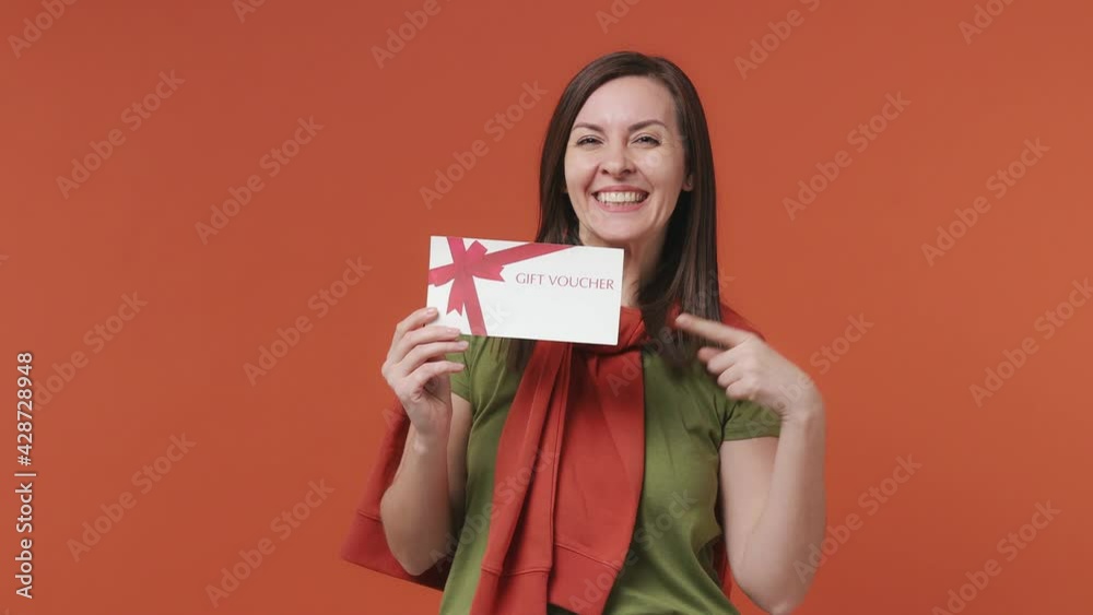 Surprised shocked happy woman 30s years old wears basic casual olive green khaki t-shirt hold in hand gift certificate voucher for store doing winner gesture isolated on bright orange color background Surprised shocked happy woman 30s years old wears basic casual olive green khaki t-shirt hold in hand gift certificate voucher for store doing winner gesture isolated on bright orange color background