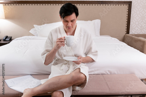 Good looking male after morning shower with a cup tasty coffee with a bathrobe. Handsome young man in bathrobe with cup of coffee. Male in bathrobe with cup of hot tea in bedroom.