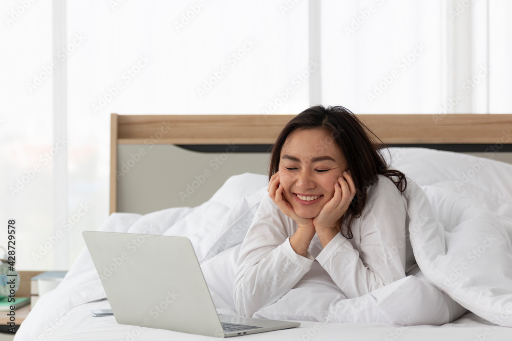 Young Asian female laying on bed using notebook computer. Happy female using laptop at home in bedroom. Working from home in quarantine lockdown. Women watching movie on laptop lying in bed. Young Asian female laying on bed using notebook computer. Happy female using laptop at home in bedroom. Working from home in quarantine lockdown. Women watching movie on laptop lying in bed.
