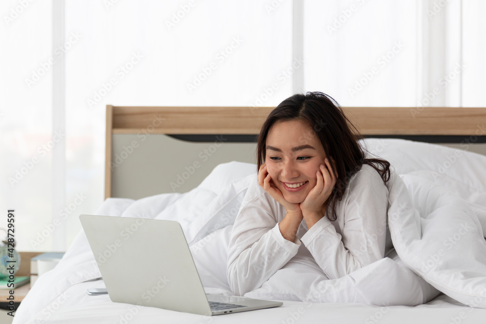 Young Asian female laying on bed using notebook computer. Happy female using laptop at home in bedroom. Working from home in quarantine lockdown. Women watching movie on laptop lying in bed. Young Asian female laying on bed using notebook computer. Happy female using laptop at home in bedroom. Working from home in quarantine lockdown. Women watching movie on laptop lying in bed.