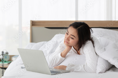 Young female laying on bed using notebook computer. Happy female using laptop at home in bedroom. Working from home in quarantine lockdown. Women watching movie on laptop lying in bed.