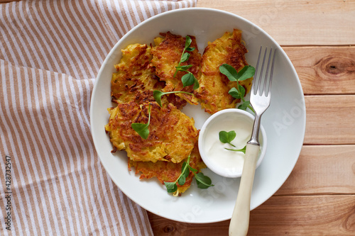 Potato pancakes or pancakes with sour cream in a plate on a wooden background. Top view.
