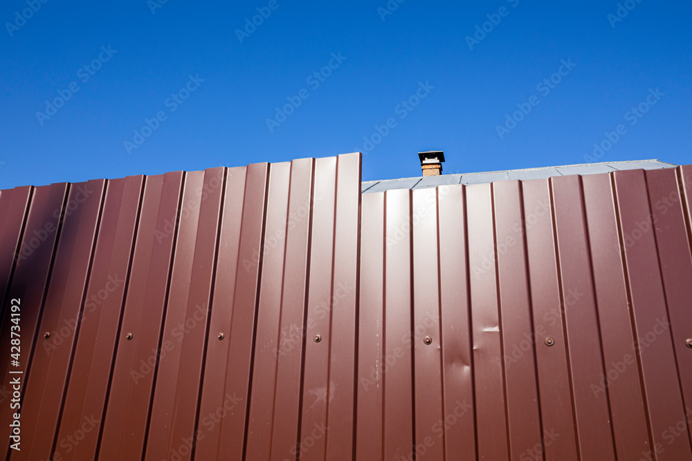 A fence made of profiled metal sheet against a blue sky. Abstract art photography.