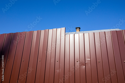 A fence made of profiled metal sheet against a blue sky. Abstract art photography.