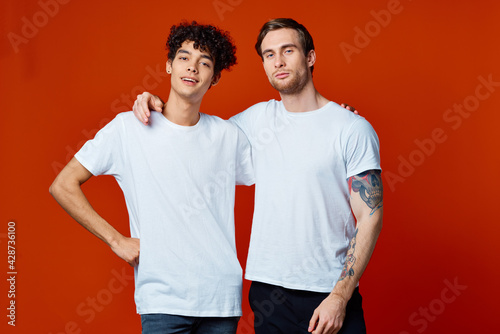 two friends in white t-shirts hugs communication red background