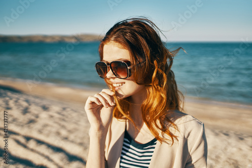 happy red-haired woman in beige jacket and t-shirt on the sand near the sea in the mountains © SHOTPRIME STUDIO