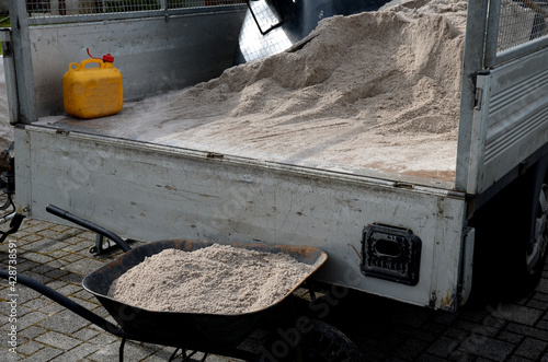 after pruning a bunch of lawn, gardeners apply silica white sand. for better structure and airiness against grass mold. load on a wheelbarrow from the body of a truck photo