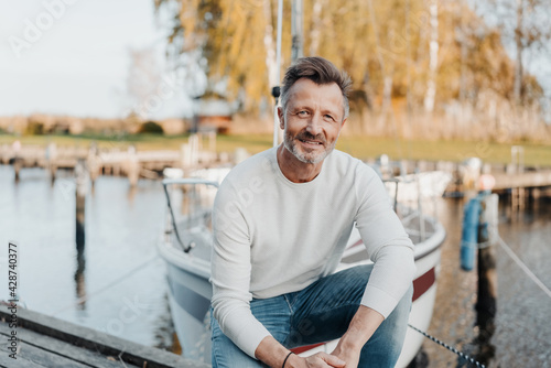 Photography Relaxed attractive man squatting on a jetty in front of his yacht